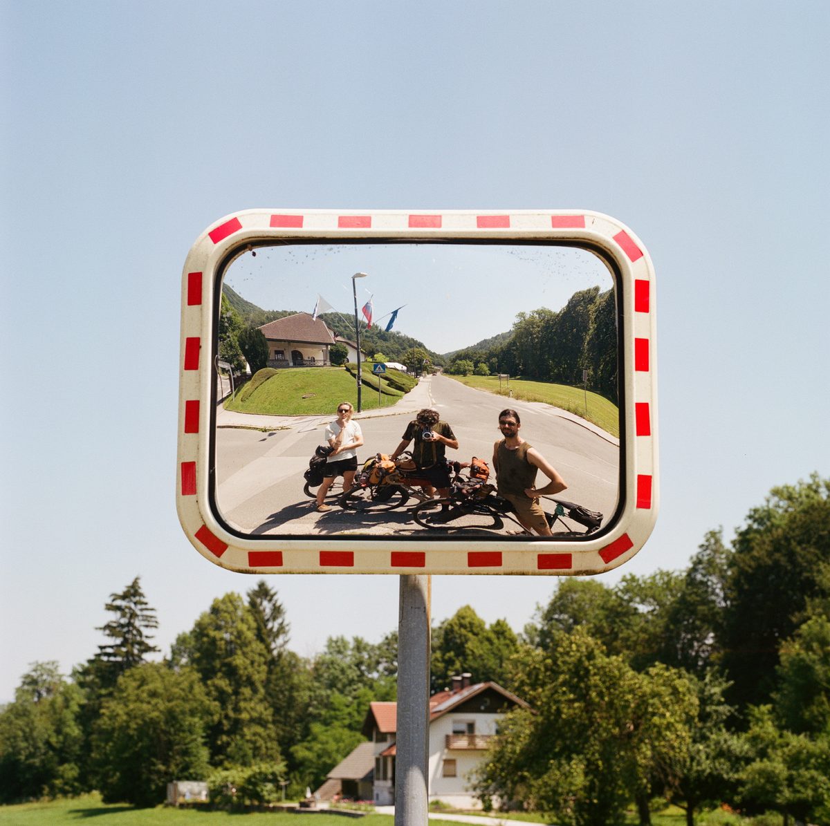 Three friends with loaded bikes, reflected in a roadside mirror