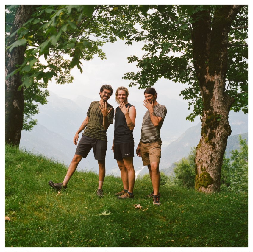 Three friends waving from a green hillside in Slovenia