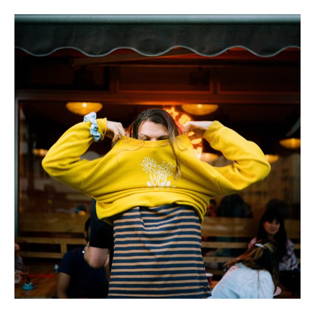 Someone pulling a yellow jumper over their head outside a bar