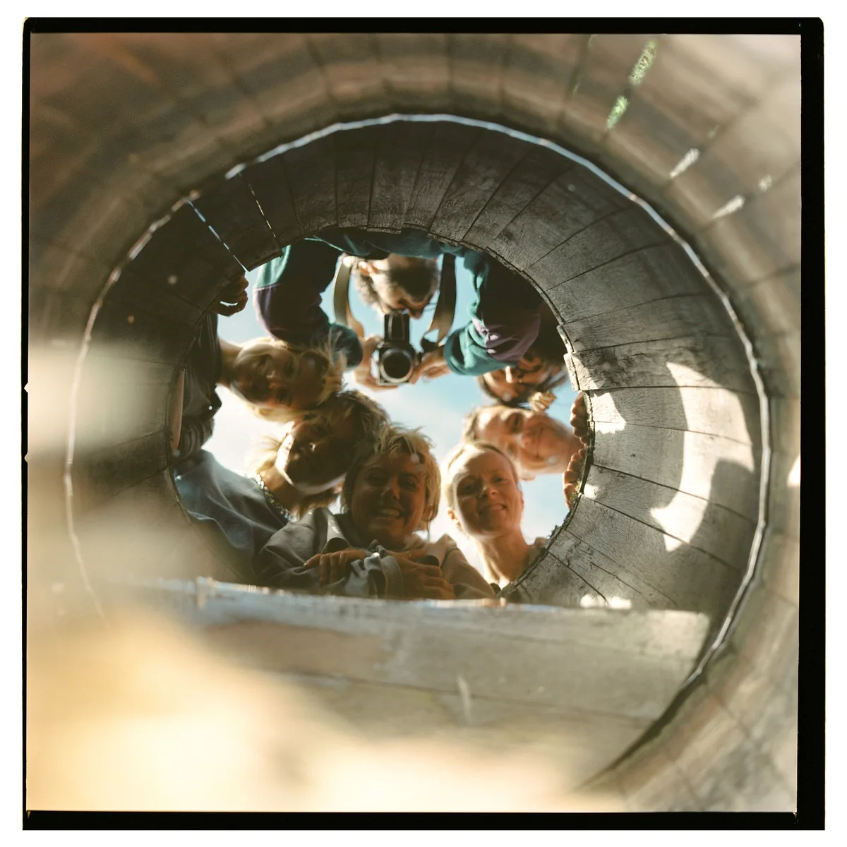 Friends looking down into a circular wooden opening, with a camera between them
